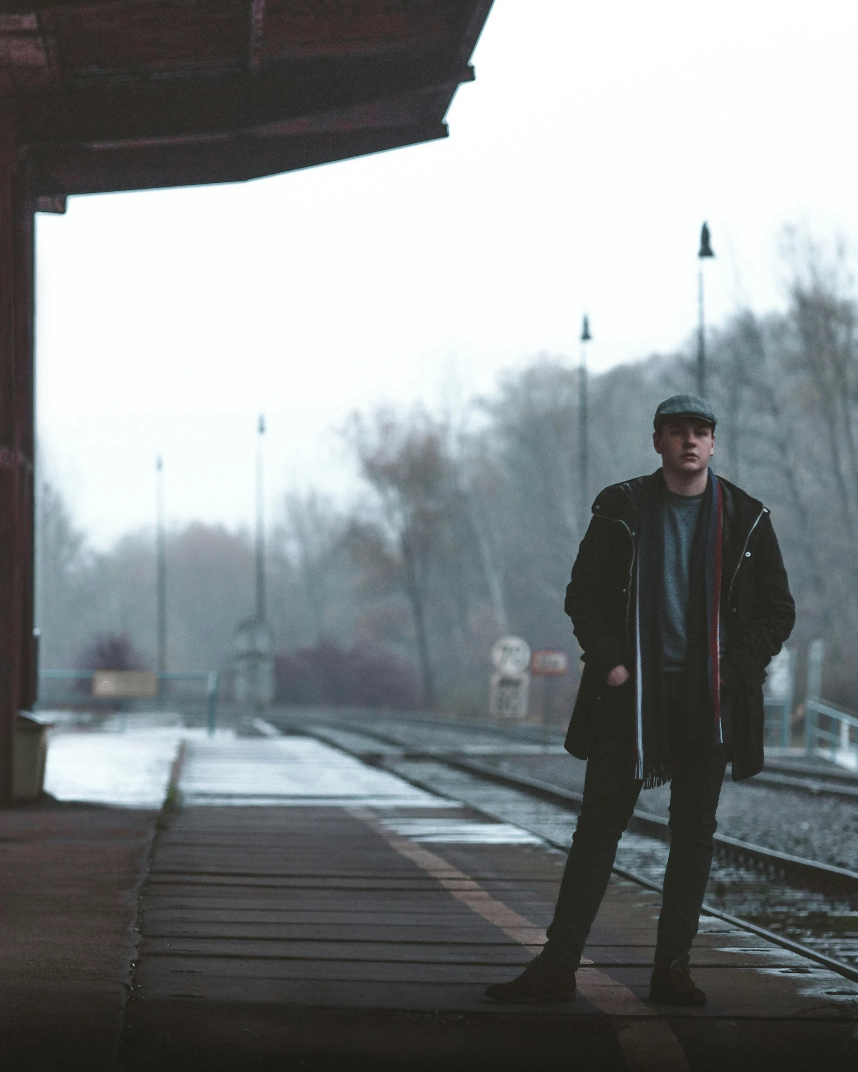 a man standing in front of a train station, by Emma Andijewska, overcast! cinematic focus, non-binary, liam, a cold