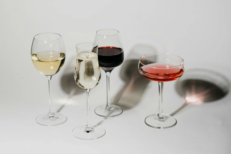 a group of wine glasses sitting next to each other, decadence, on a pale background, with a drink, curated collection