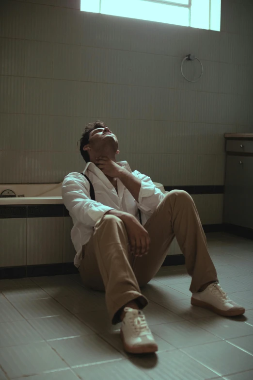 a man sitting on a bench in a bathroom, an album cover, by Elsa Bleda, pexels, he has a devastated expression, clothed in white shirt, hospital, ( ( theatrical ) )