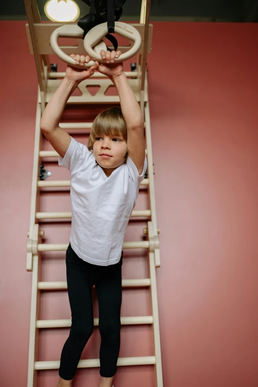 a little boy that is standing on a ladder, by Nina Hamnett, arabesque, in a gym, high-quality photo, upper body image, square