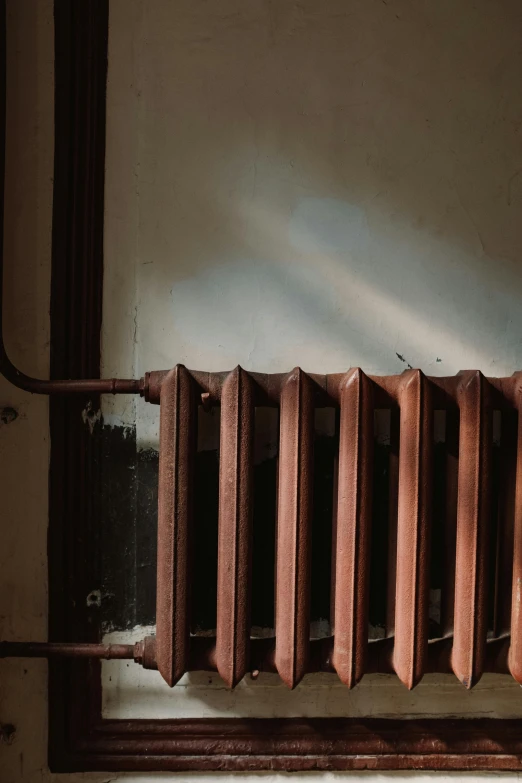 a radiator sitting next to a window in a room, an album cover, inspired by Elsa Bleda, pexels contest winner, old copper pipes, brown, shadows, low quality photo