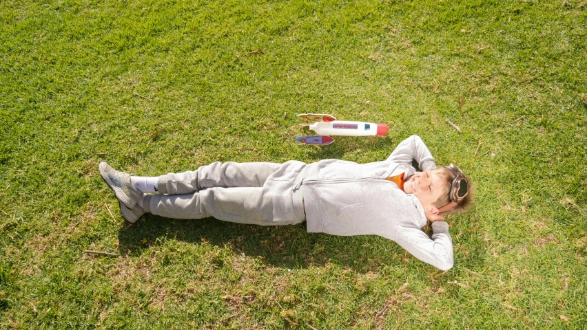 a man laying on top of a lush green field, holding a rocket, profile image, in a sun lounger, wearing track and field suit