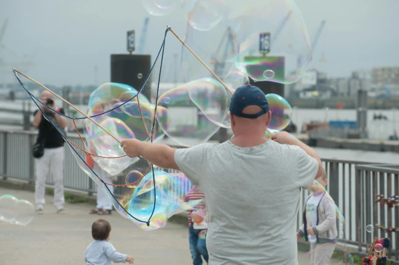 a man holding a bunch of soap bubbles, kinetic art, set sail, at the waterside, families playing, photograph taken in 2 0 2 0