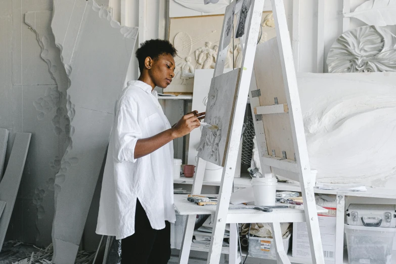 a woman that is standing in front of a easel, by Meredith Dillman, pexels contest winner, arbeitsrat für kunst, kara walker james jean, wearing lab coat and a blouse, drawing architecture, on a canva