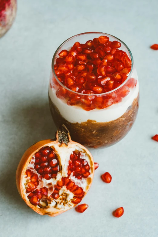 a dessert sitting on top of a table next to a pomegranate, inside a glass jar, the god of oatmeal, fall vibrancy, pro - vida