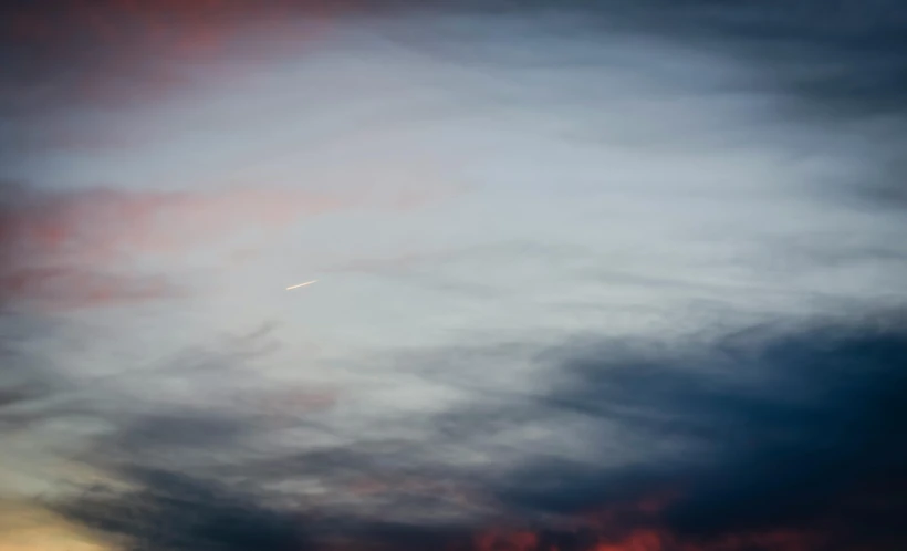 a plane flying through a cloudy sky at sunset, inspired by Jan Rustem, minimalism, shooting star, archival pigment print, muted blue and red tones, multicoloured