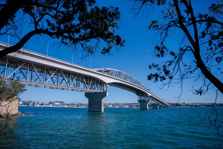 a bridge over a large body of water, by Simon Marmion, unsplash, hurufiyya, clear blue skies, te pae, surrounding the city, under bridge