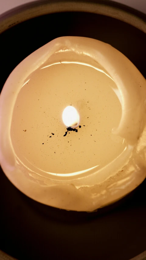 a lit candle in a bowl on a table, inspired by Marina Abramović, glowing spores flying, close-up from above, round-cropped, made of glazed