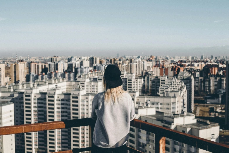 a woman standing on a balcony overlooking a city, a picture, trending on unsplash, female streetwear blogger, sparsely populated, highrise buildings, panoramic view of girl