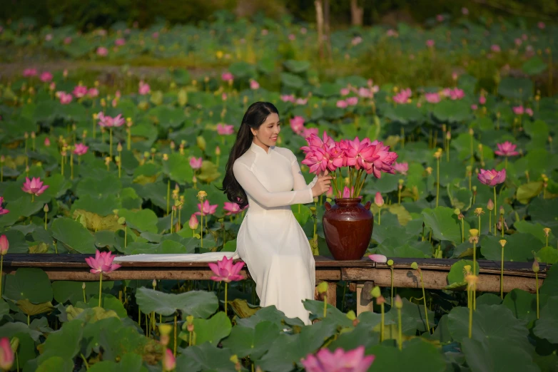 a woman in a white dress sitting in a field of pink flowers, inspired by Cui Bai, pexels contest winner, visual art, waterlily pads, ao dai, avatar image, standing in a botanical garden