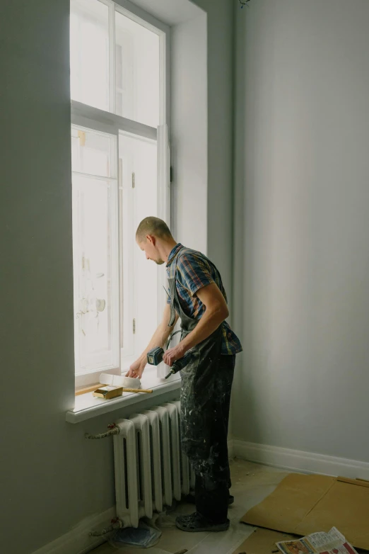 a man standing next to a window in a room, paint, digging, professional image, trending photo