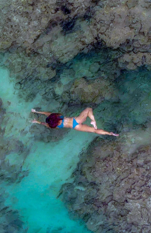 a woman laying on top of a rock next to a body of water, delicate coral sea bottom, overhead birdseye view, kailee mandel, in flight