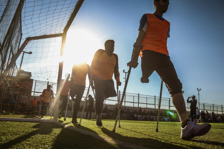 a group of young men playing a game of soccer, by Youssef Howayek, unsplash, crutches, holding a cane, blinding bright sun, prosthetic limbs