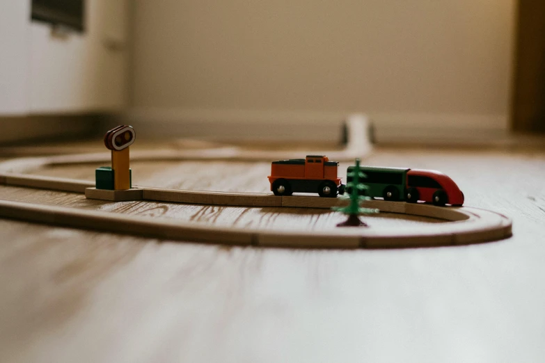 a toy train set sitting on top of a wooden floor, by Emma Andijewska, pexels contest winner, a round minimalist behind, wooden banks, let's play, unobstructed road