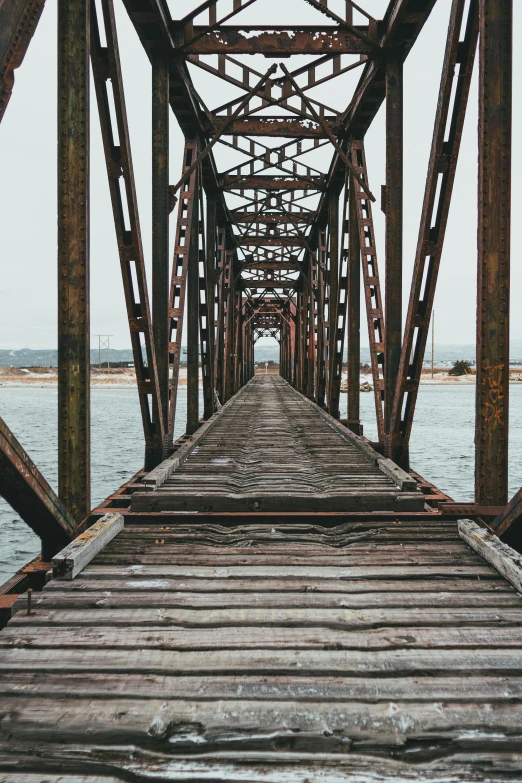 a long wooden bridge over a body of water, an album cover, unsplash contest winner, rusty metal towers, 2 5 6 x 2 5 6 pixels, rust and corrosion, truss building