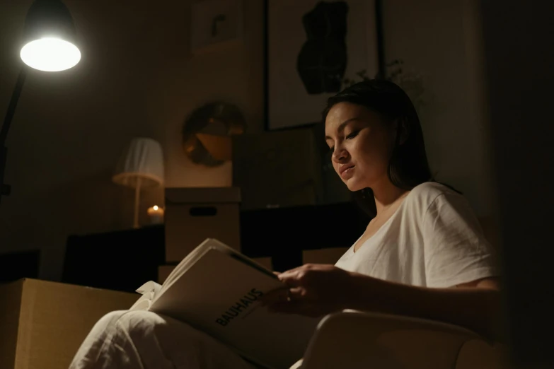 a woman sitting in a chair reading a book, pexels contest winner, night time footage, wearing a nightgown, minimalist cinematic lighting, cindy avelino