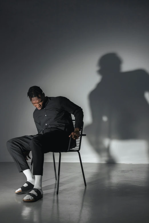 a man sitting on a chair in a dark room, an album cover, trending on pexels, portrait casting long shadows, black man, action pose : : spotlight, 3d shadowing effect