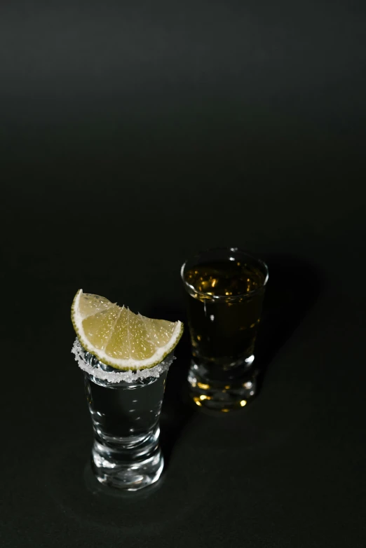 two shot glasses filled with liquid and a slice of lemon, a still life, pexels, mexican, mid 2 0's female, police shot, sprites
