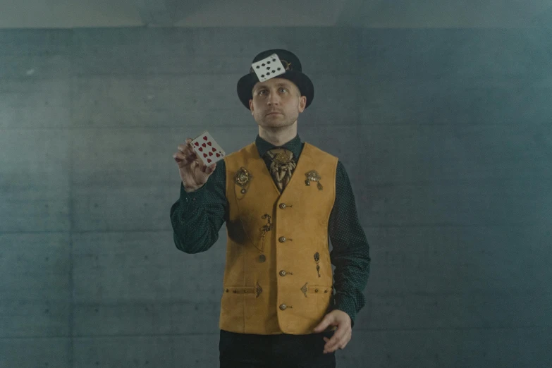 a man in a yellow vest holding playing cards, a portrait, by Emma Andijewska, pexels contest winner, surrealism, wearing steampunk top hat, still from the film, square, cardistry