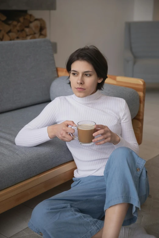 a woman sitting on a couch holding a cup of coffee, concerned, in white turtleneck shirt, premium, julia sarda