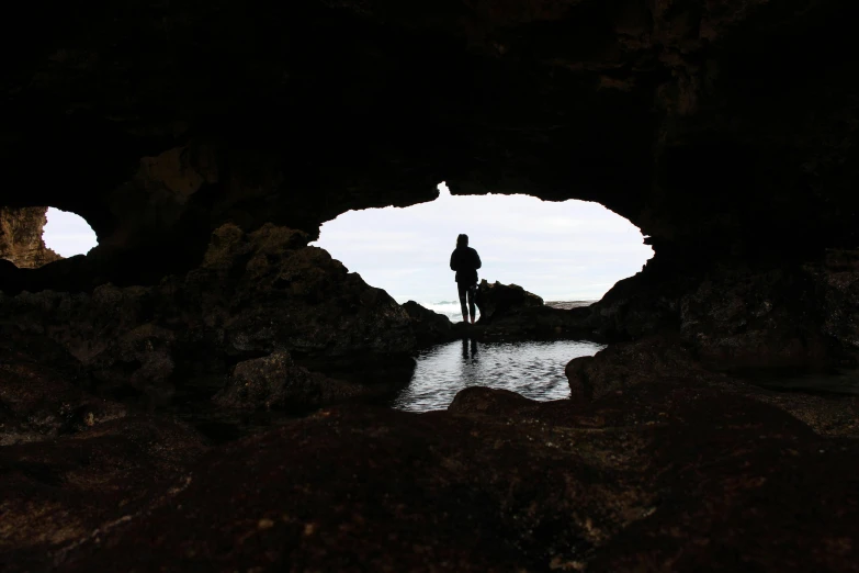 a couple of people standing inside of a cave, by Jessie Algie, pexels contest winner, lone silhouette in the distance, rock pools, a person standing in front of a, te pae