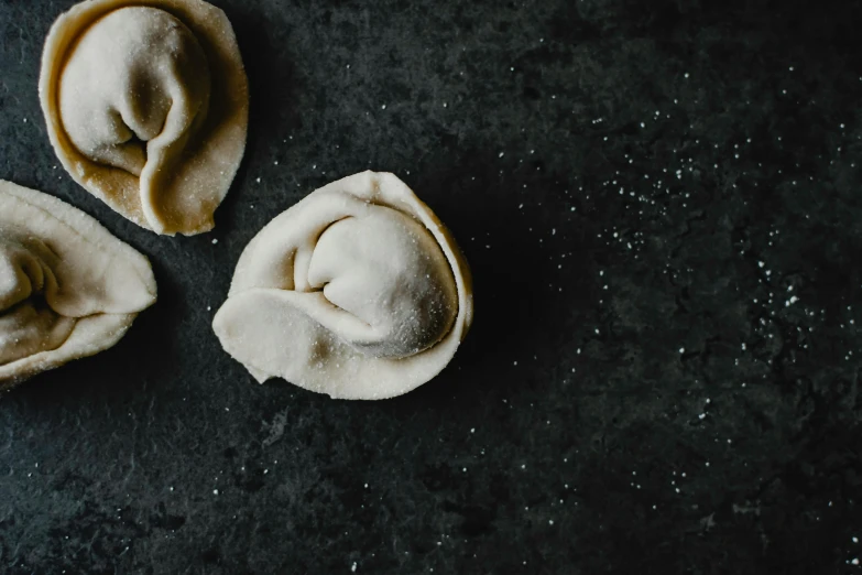 a couple of dumplings sitting on top of a table, unsplash, process art, background image, twisted shapes, recipe, grey