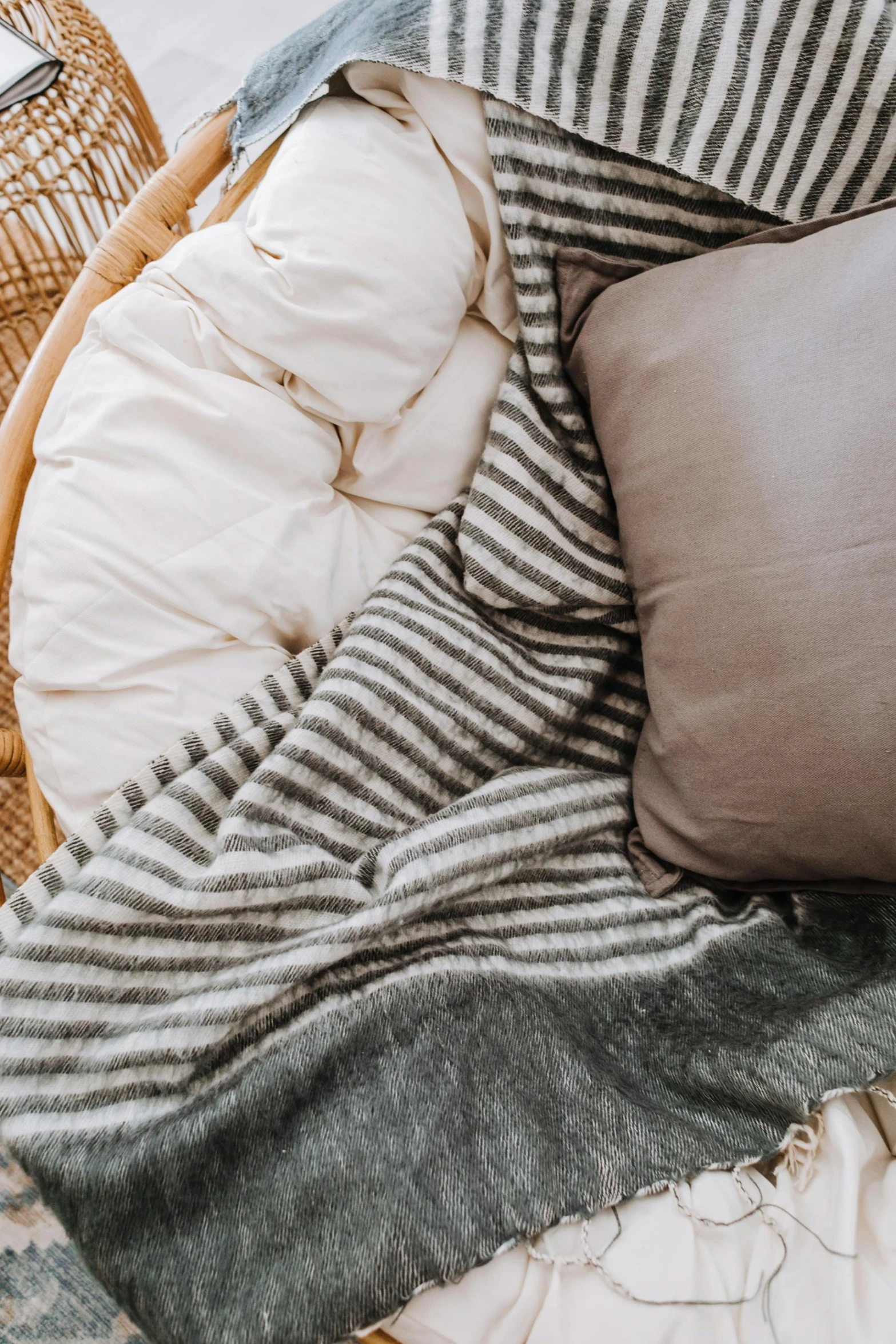 a basket filled with pillows and blankets on top of a bed, by Adam Marczyński, unsplash, striped, detailed product image, charcoal and champagne, laying down