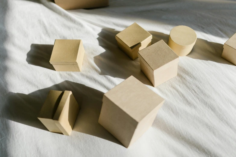 a group of wooden blocks sitting on top of a bed, inspired by Rachel Whiteread, trending on unsplash, visual art, square shapes, beige, shadows, sitting on a mocha-colored table