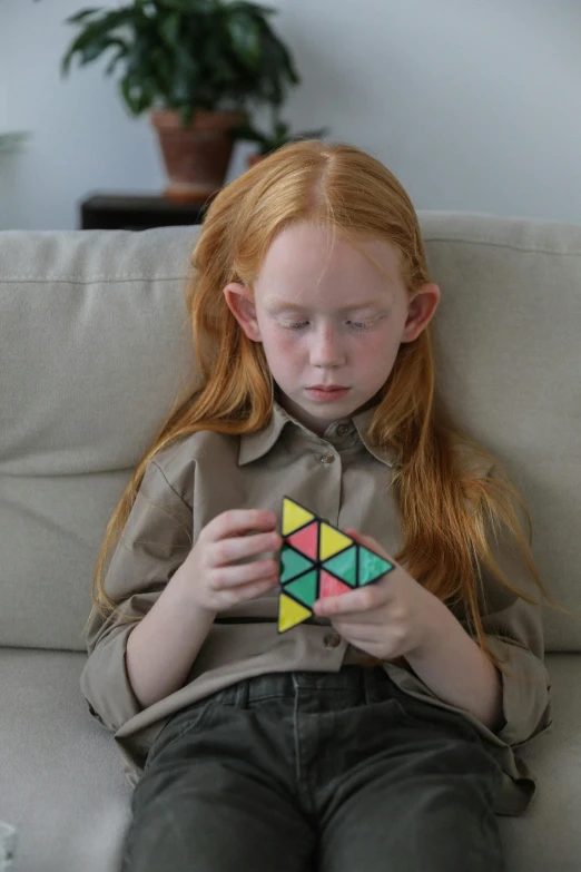 a little girl sitting on a couch playing with a rubik cube, a jigsaw puzzle, by Thomas Furlong, kinetic art, sadie sink, flat triangles, 8k 50mm iso 10, gen z