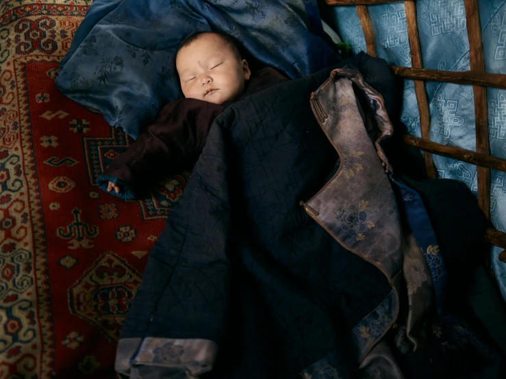 a baby is wrapped up in a blanket, by Elsa Bleda, unsplash contest winner, cloisonnism, gold brocaded dark blue clothes, omar shanti himalaya tibet, sleepers, dezeen