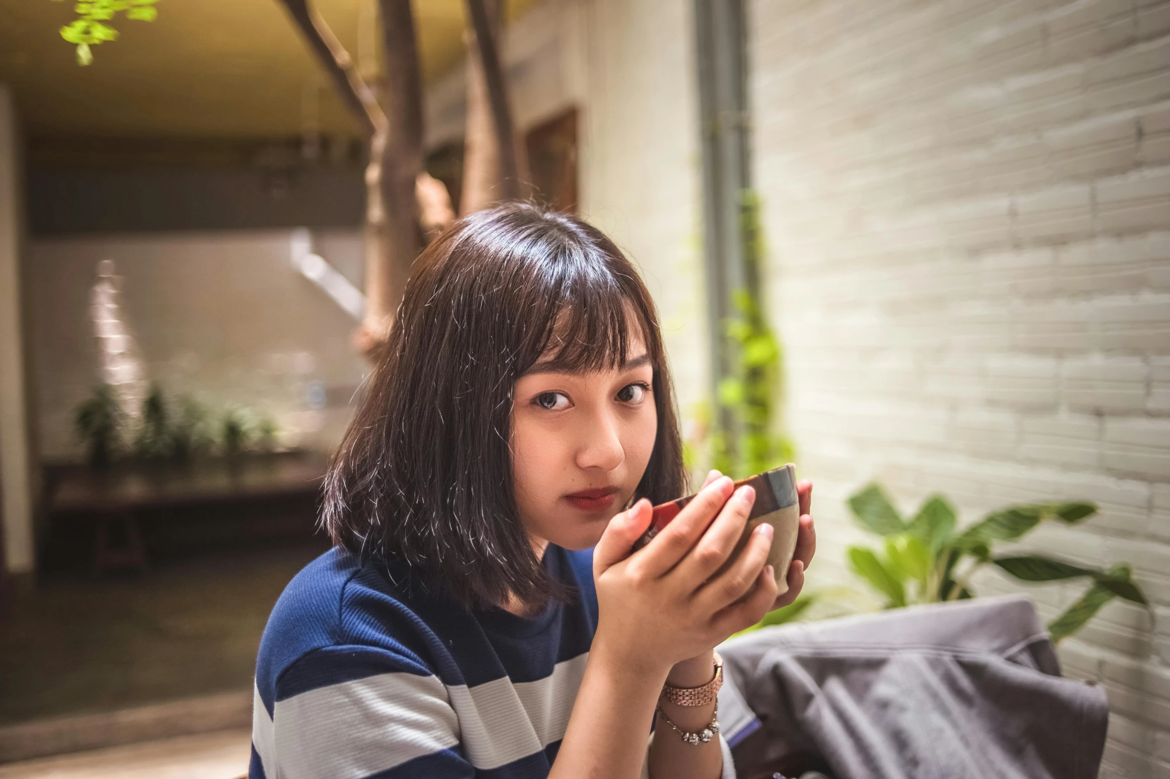 a woman sitting on a couch holding a cell phone, pexels contest winner, shin hanga, is ((drinking a cup of tea)), young cute wan asian face, avatar image, eating outside