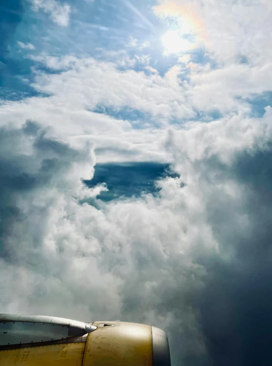 an airplane that is flying in the sky, an album cover, inspired by Storm Thorgerson, unsplash, extreme fluffy clouds, high - angle view, pareidolia, battered