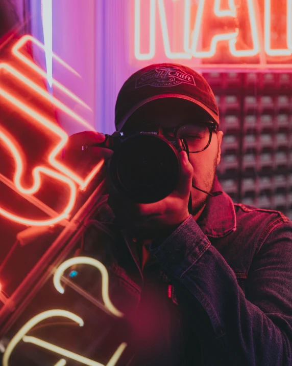 a man taking a picture of a neon sign, pexels contest winner, looking into camera, bisexual lighting, wearing sunglasses and a cap, gif