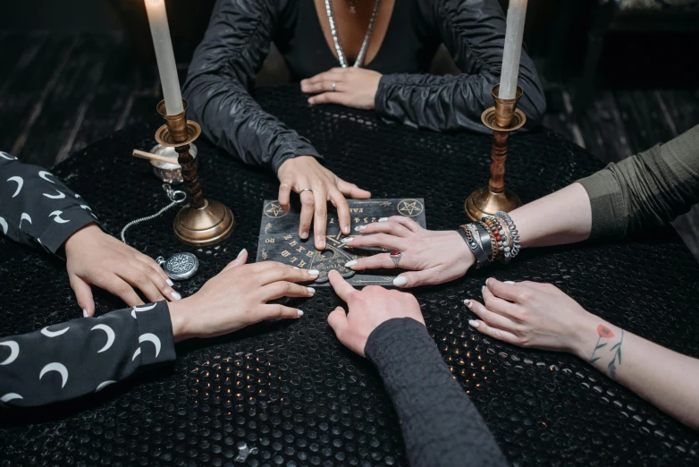 a group of people sitting around a table with candles, an album cover, by Julia Pishtar, trending on pexels, wizard shuffling cards, black hands with black claws, hypnosis, tabletop game board