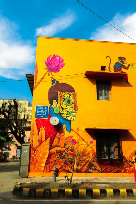 a building with a mural on the side of it, graffiti art, inspired by Bhupen Khakhar, street art, yellow and ornage color scheme, mexico, kalighat flowers, with an intricate