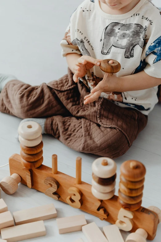 a little boy sitting on the floor playing with wooden blocks, by Emma Andijewska, pexels contest winner, art toys on a pedestal, rings, organic shapes, repeating pattern