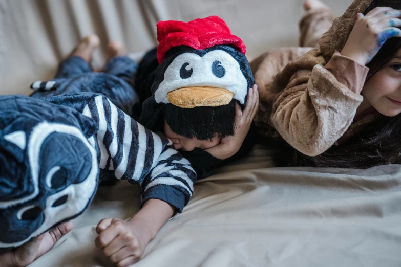 a couple of kids laying on top of a bed, a cartoon, trending on pexels, anthropomorphic penguin, costume, head in hands, outfit photograph