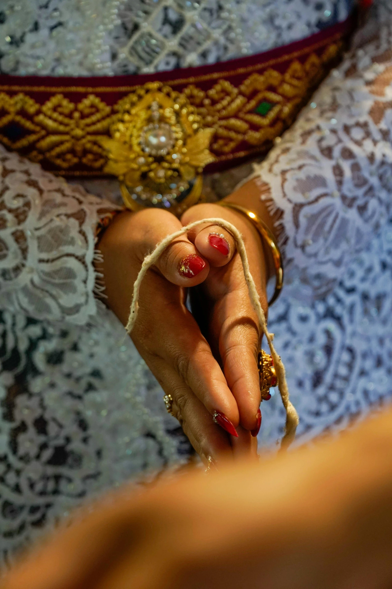 a close up of a person holding a ring, dressed in a sari, legs intertwined, intricate golden threads, exposed toes