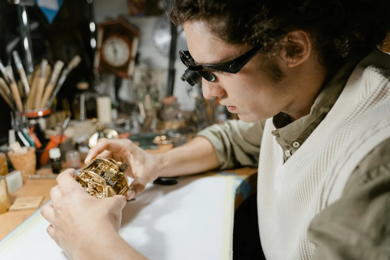 a man sitting at a table working on something, a hyperrealistic painting, trending on pexels, wearing victorian brass goggles, small manufacture, plating, holding gold watch