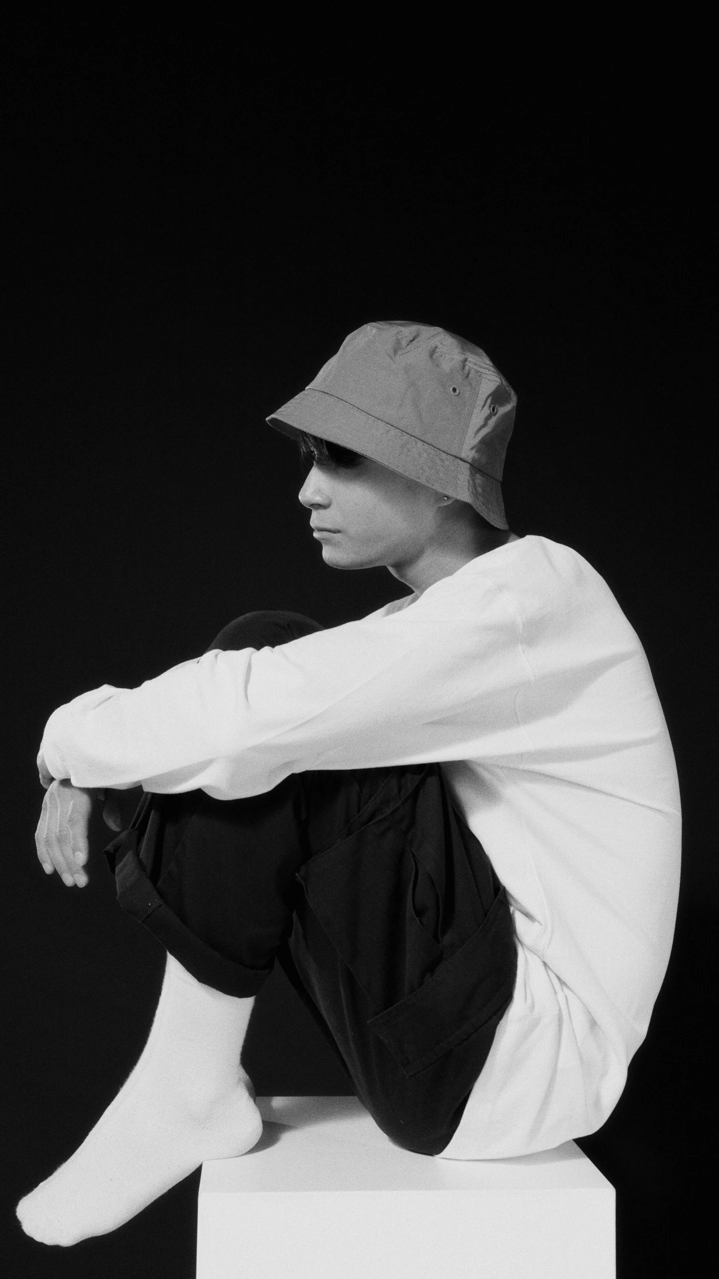 a man sitting on top of a white box, a black and white photo, unsplash, realism, baggy clothing and hat, wearing a tracksuit, androgynous, profile image