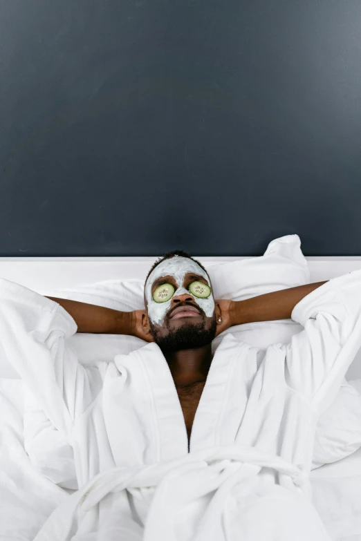 a man laying in bed with a mask on his face, trending on pexels, happening, black face, conde nast traveler photo, spa, on a gray background