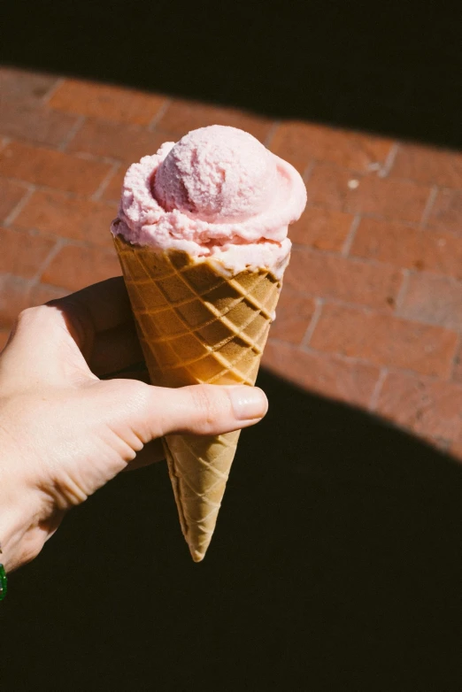 a person holding an ice cream cone in their hand, pink concrete, boston, feature, epicurious