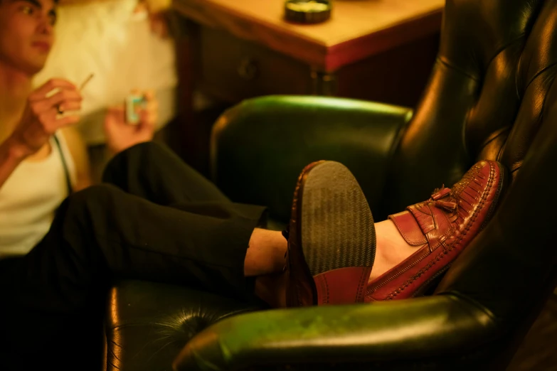 a close up of a person sitting in a chair, inspired by Harrington Mann, trending on pexels, renaissance, duck shoes, in a pub, impeccably dressed, reclining