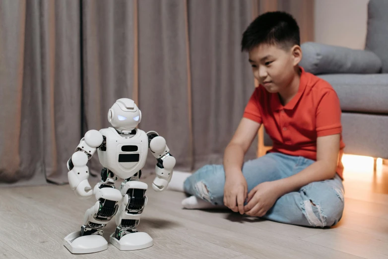 a boy sitting on the floor next to a robot, pexels contest winner, asian male, a person standing in front of a, animated, at home