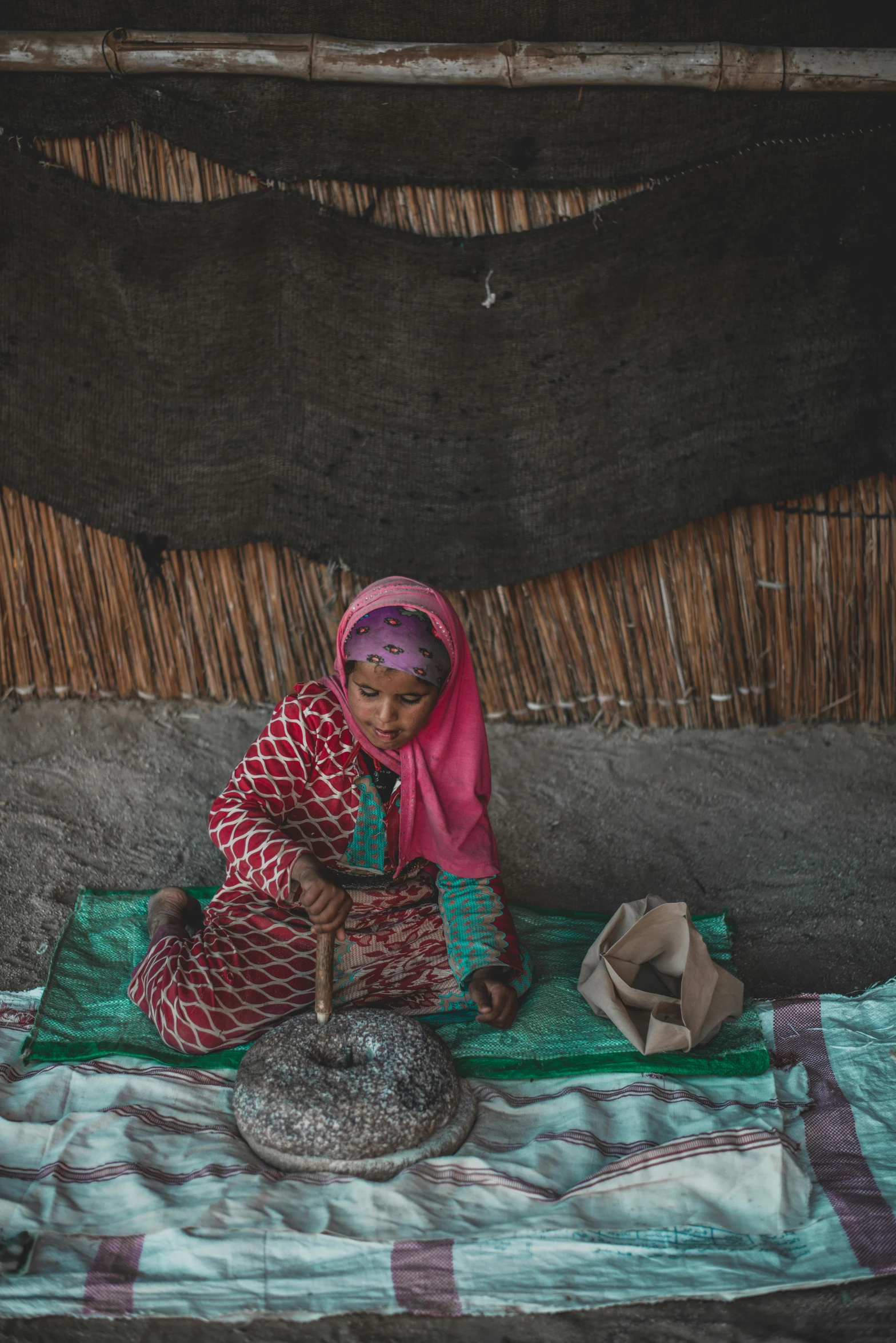 a woman that is sitting on a blanket, inspired by Steve McCurry, unsplash contest winner, hurufiyya, working in the forge, somali attire, clay material, makeshift houses