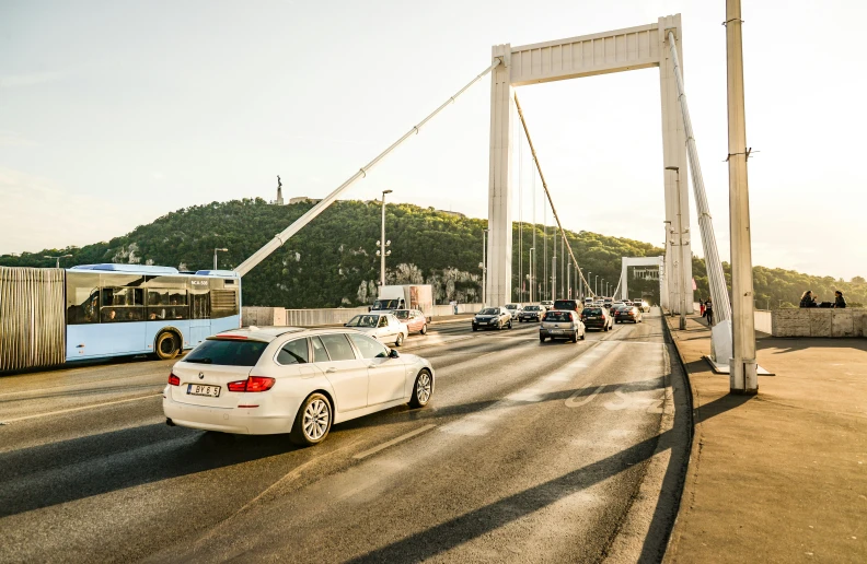 a white car driving across a bridge next to a bus, by Matija Jama, pexels contest winner, happening, istanbul, square, super high resolution, bmw