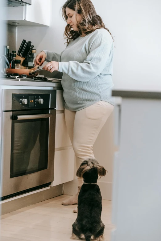 a woman standing in a kitchen next to a dog, pexels contest winner, steaming food on the stove, pregnant belly, gif, profile image