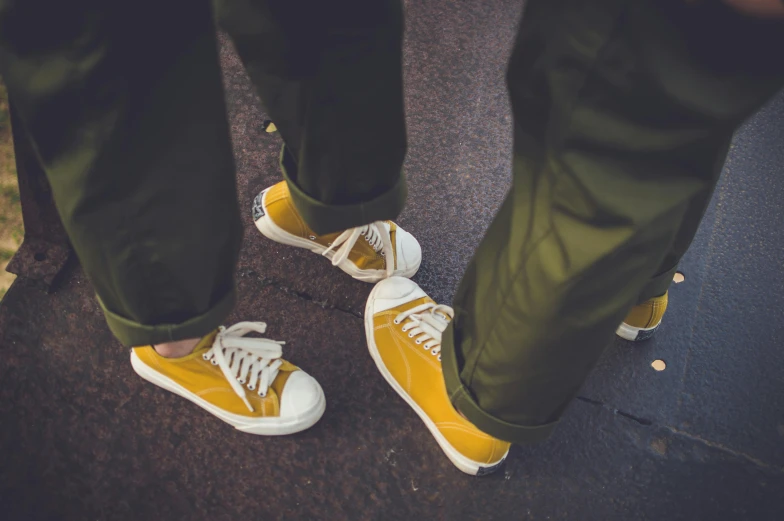 a close up of a person standing on a skateboard, by Nina Hamnett, happening, yellow and olive color scheme, man and woman walking together, gum rubber outsole, gold and white