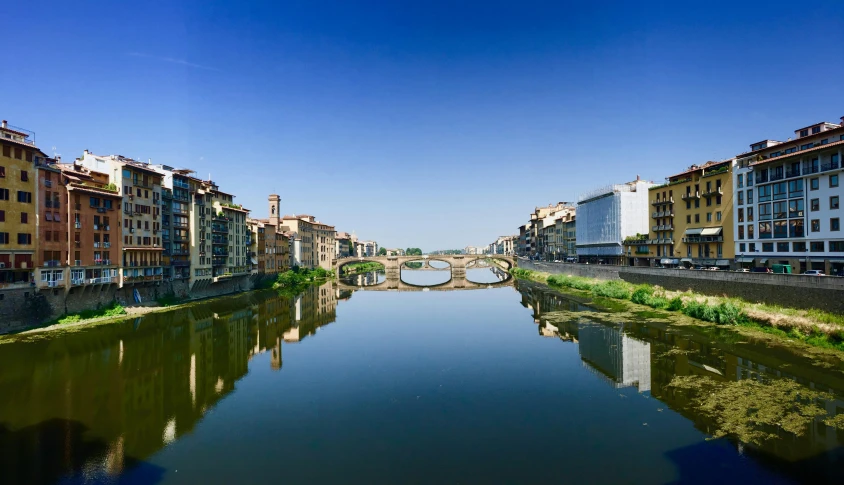 a river running through a city next to tall buildings, by Patrick Pietropoli, pexels contest winner, renaissance, clear blue skies, florentine school, metallic bridge, a photo of a lake on a sunny day