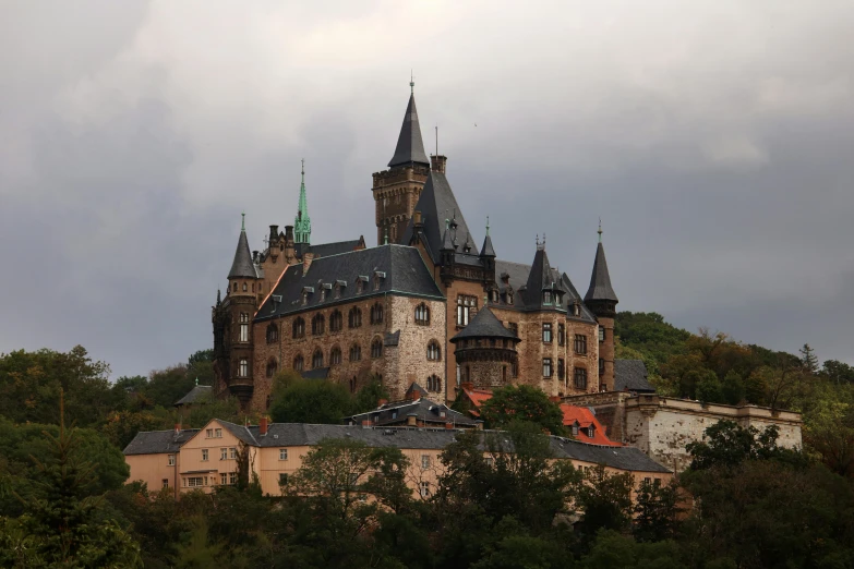 a castle sitting on top of a lush green hillside, a photo, by Breyten Breytenbach, pexels contest winner, art nouveau, black domes and spires, brown, cornell, gray